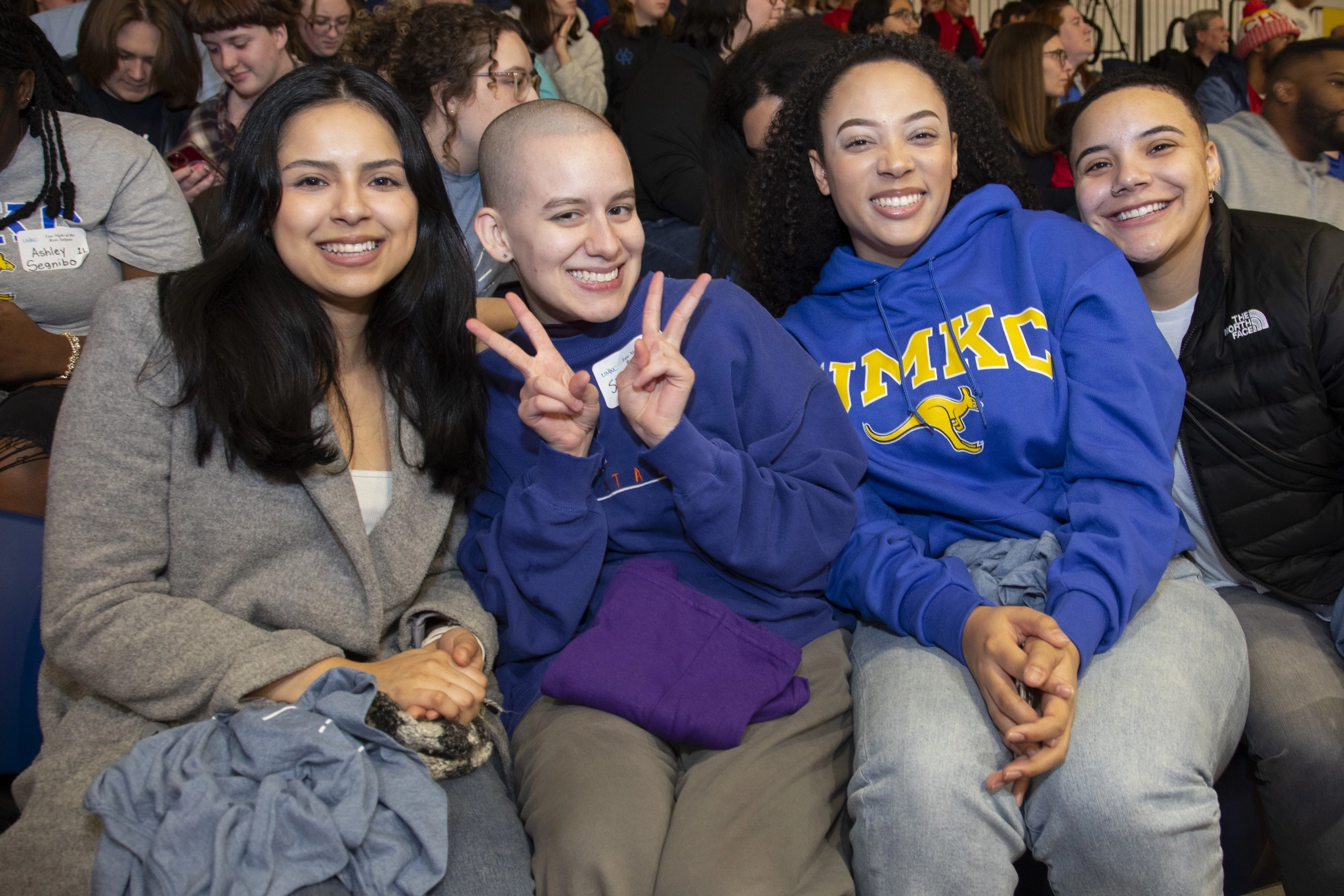 Four students pose for photo. One student second from left holds up peace signs. The person to their right is wearing a UMKC shirt.